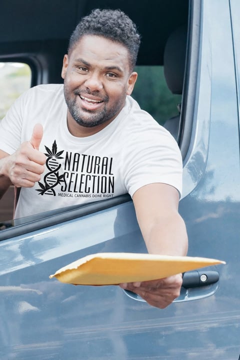 Man leaning out of a vehicle window wearing a Natural Selection shirt and giving a thumbs up while holding a large knife.